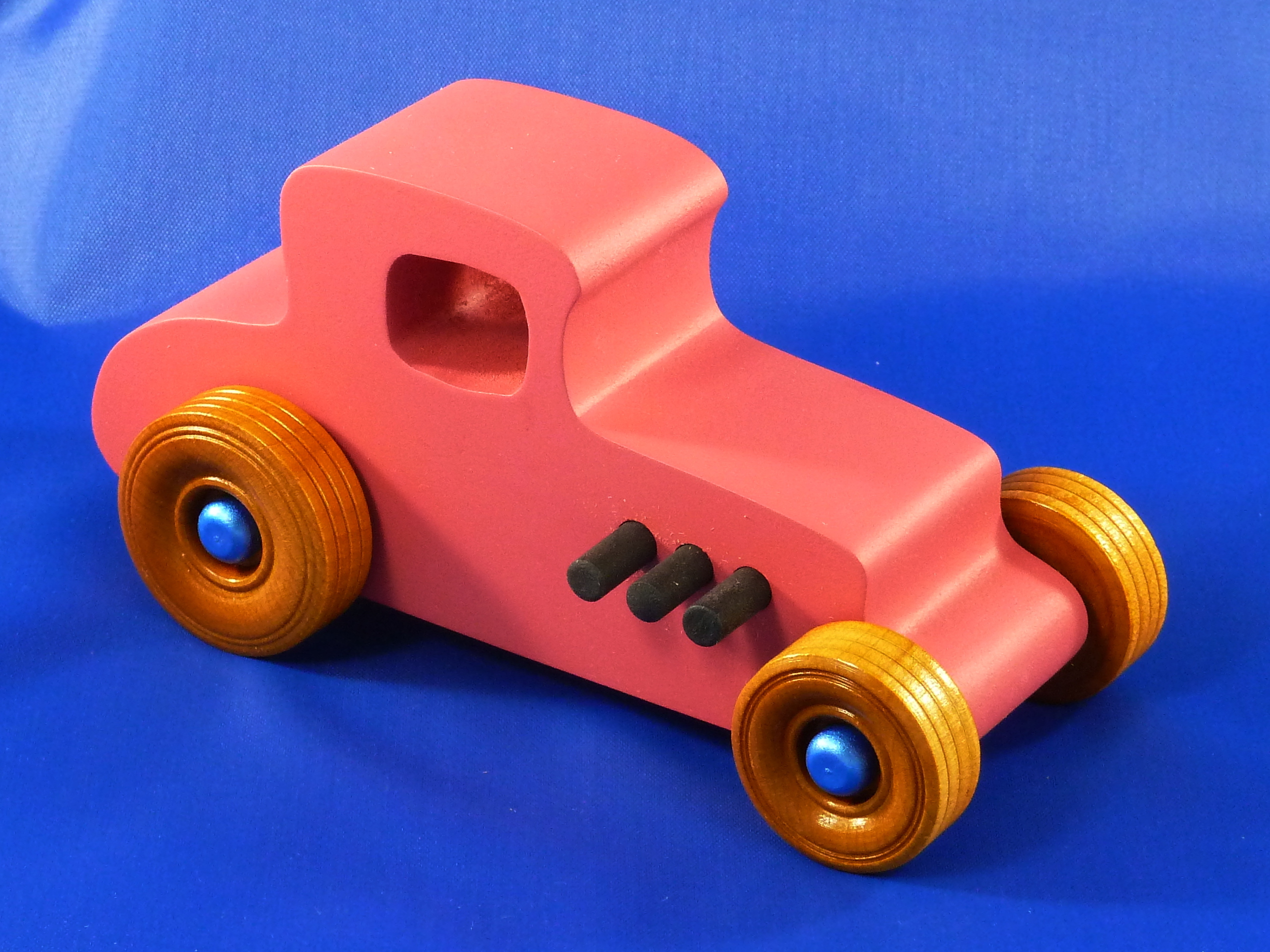 Handmade wooden toy car '27 T-Coupe Hot Rod painted pink with metallic sapphire blue, black trim, and nonmarring amber shellac wheels.