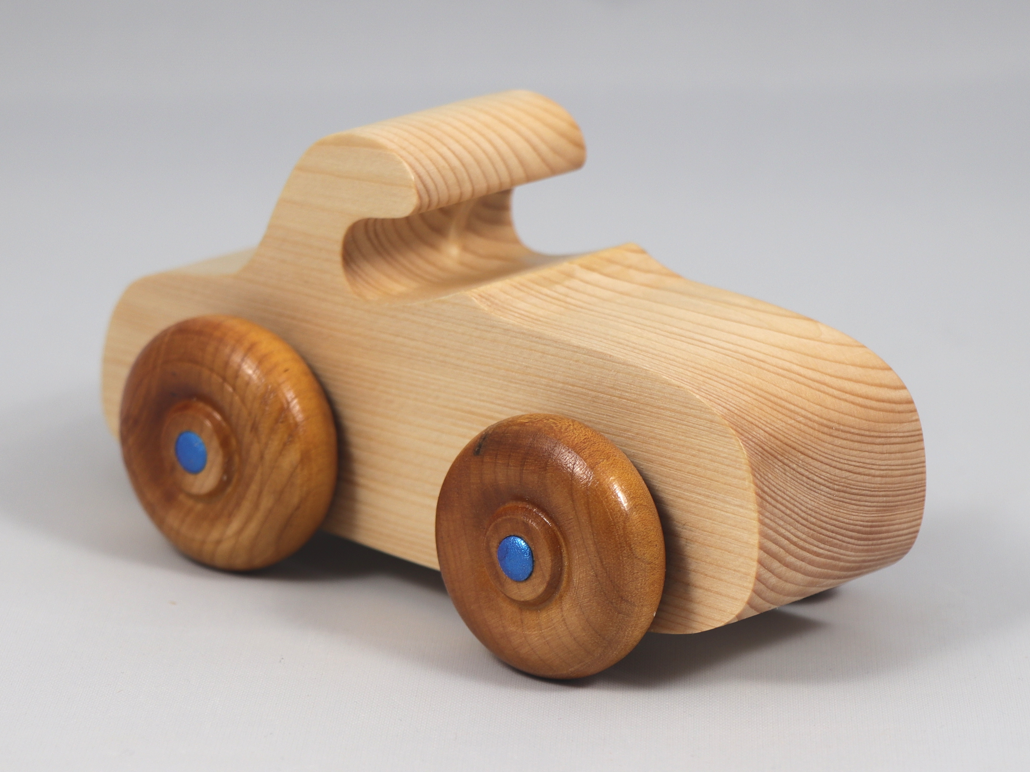 Handmade wooden toy car. The body is finished with clear shellac, and the wheels are finished with amber shellac. The hubs are painted with metallic sapphire blue trim.